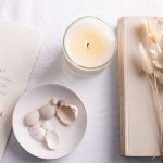 Lit non-toxic candle beside an open book, dried flowers, and handwritten journal—evoking calm, intention, and mindful living.