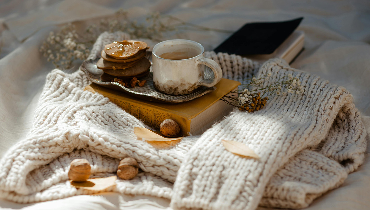 Cosy autumn coffee and biscuits on a knitted blanket in warm neutral tones.