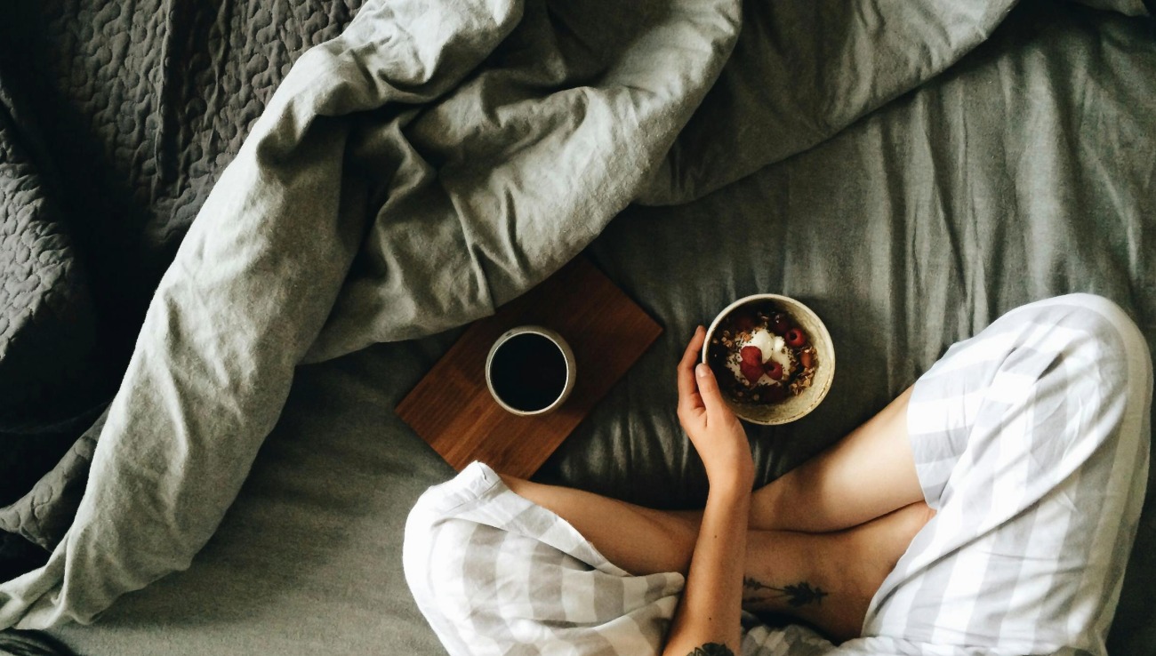 person sitting in bed with coffee and breakfast bowl symbolising rest, slowness, and gentle living with chronic illness