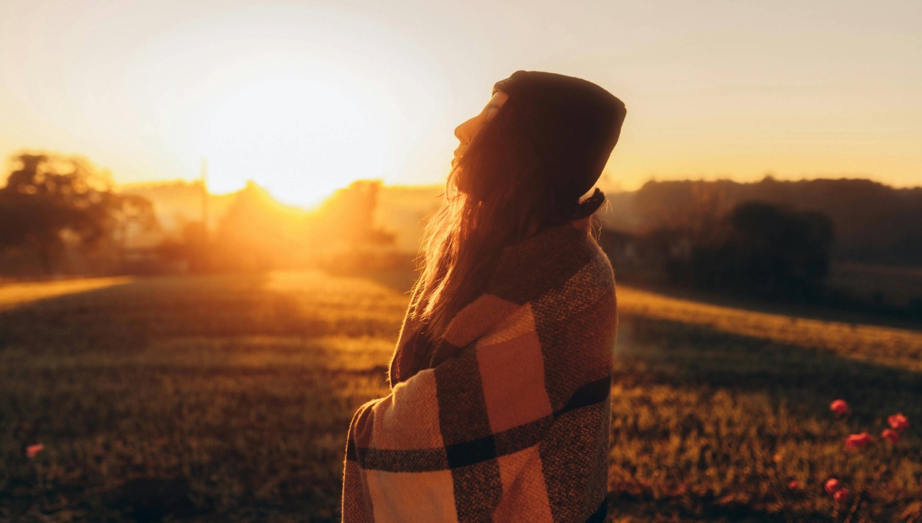 woman wrapped in a blanket at sunrise representing hope, warmth, and gentle living with chronic illness