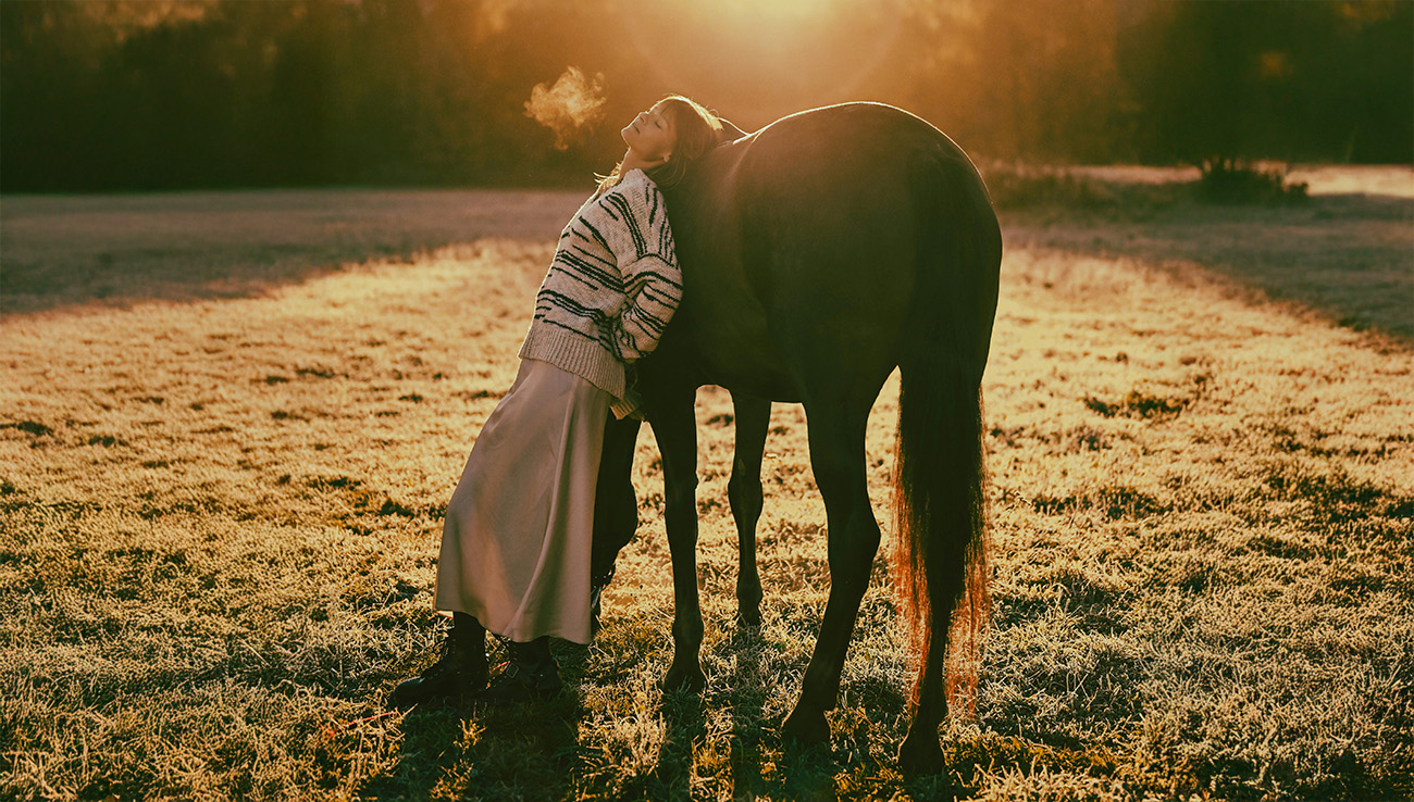 a girl leaning against a horse in a field